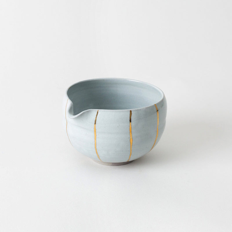 From Tetang Studio, this handcrafted ceramic matcha bowl from Chiang Mai features a light gray finish with gold-repaired cracks and a small pouring spout, shown on a plain white background.