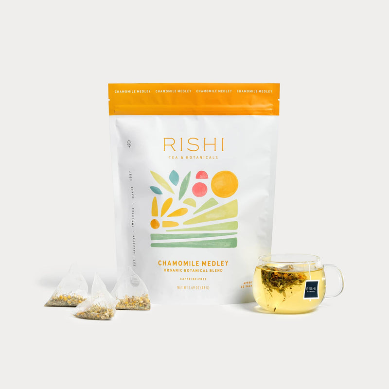 A bag of Rishi Tea & Botanicals Chamomile Medley, three pyramid tea bags, and a glass cup filled with this relaxing floral tea are shown on a white background.