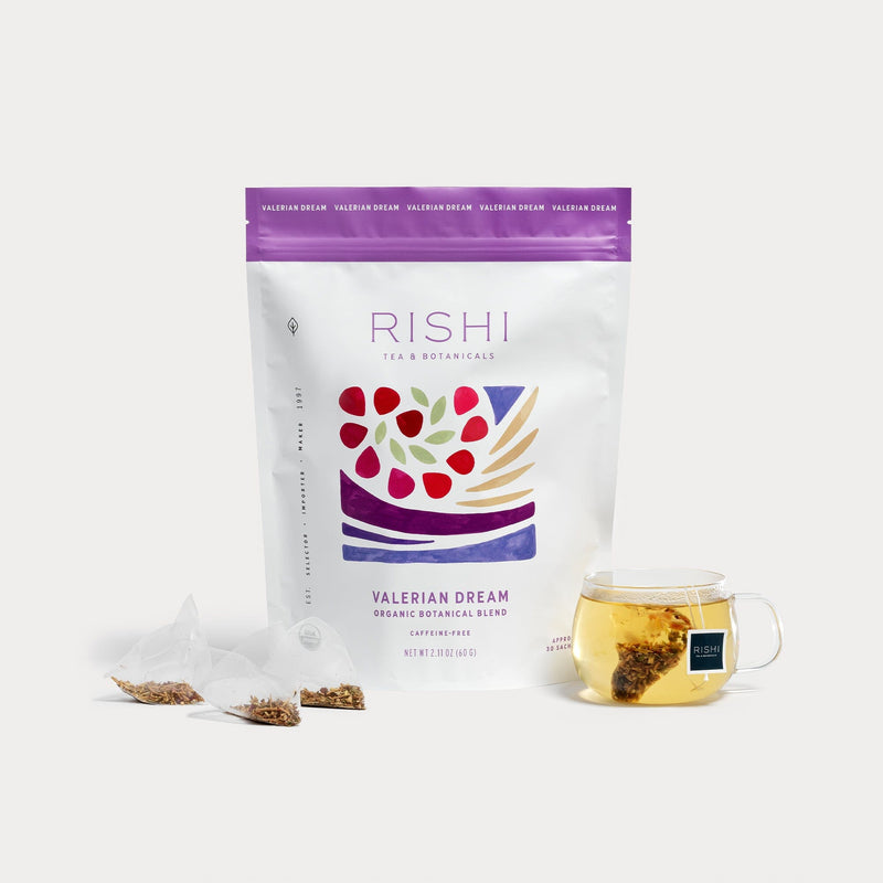 A bag of Rishi Tea & Botanicals Valerian Dream organic blend with three pyramid sachets and a glass cup of fragrant brewed tea, offering floral notes and an inviting sense of calm.