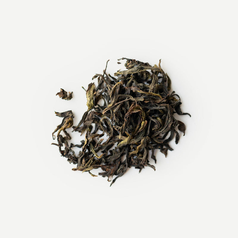 Loose dried tea leaves from Rishi Tea & Botanicals are arranged in a small pile on a white background, suggesting Wuyi oolong’s signature orchid aroma and delicate mountain minerality.
