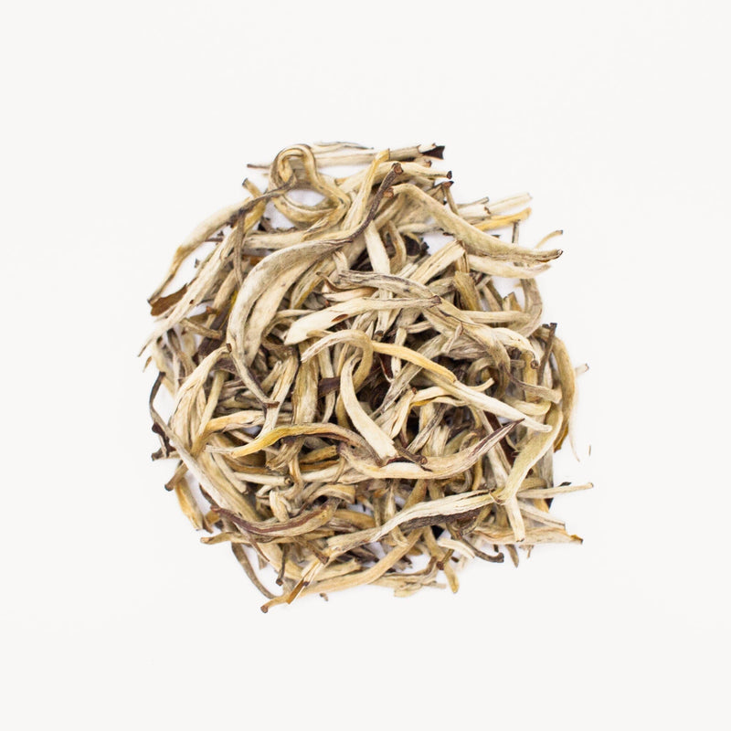 Against a plain white backdrop, a pile of dried, twisted tea leaves highlights the elegance of Rishi Tea & Botanicals' Yunnan Silver Needles.