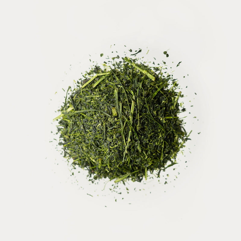 Loose, dried green tea leaves from Rishi Tea & Botanicals’ organic micro-lot shincha rest on a plain white background, showcasing the vibrant quality nurtured in Kyushu Island’s volcanic soil.