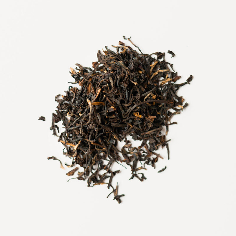 A pile of Rishi Tea & Botanicals organic Dian Hong black tea with golden tips is displayed on a white background.